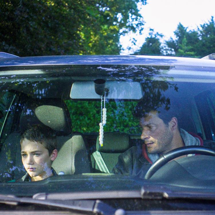 Volwassen man kijkt boos naar jongen naast hem in de auto.