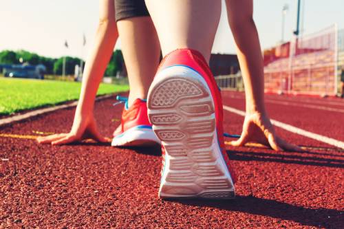 Een hardloper staat klaar voor de start op een hardloopbaan. Je ziet alleen de 2 voeten me sportschoenen.