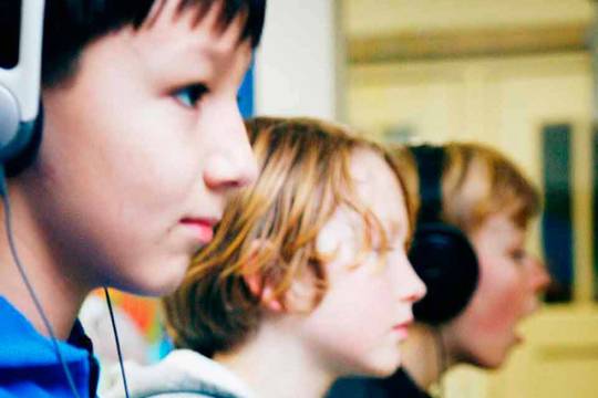 Decoratieve afbeelding: Drie jongeren met een koptelefoon aan het werk op een computer