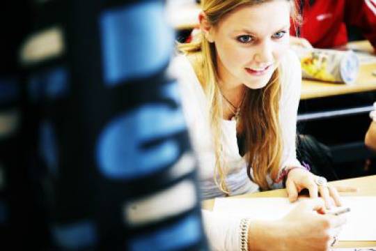 Decoratieve afbeelding: een jongere zit aan een tafel in een klas met een pen in haar hand