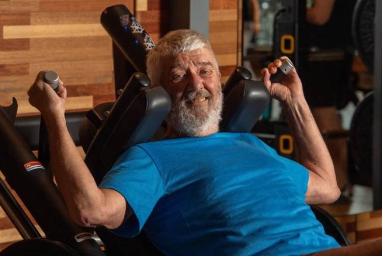 En man met grijs haar en een baard lacht en zit op een fitnessaparaat