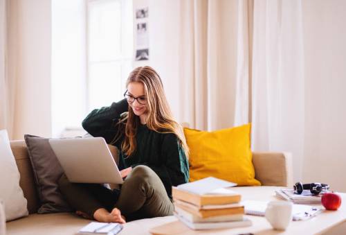En jonge vrouw zit op de bank met haar laptop