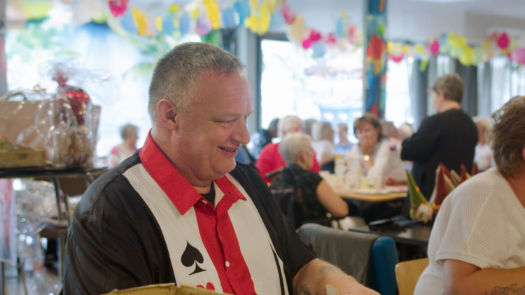 Mannelijke zestigplusser staat omringd door andere mensen in een vrolijk versierd buurthuis