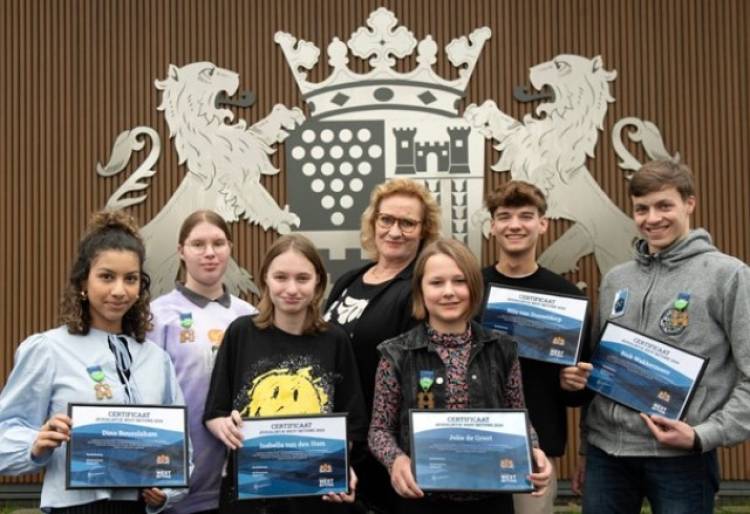 5 jongeren die een jeugdlintje hebben gekregen, staan op een rij en laten hun jeugdlintje zien. Wethouder Wil Kosterman staat achter de jongeren.