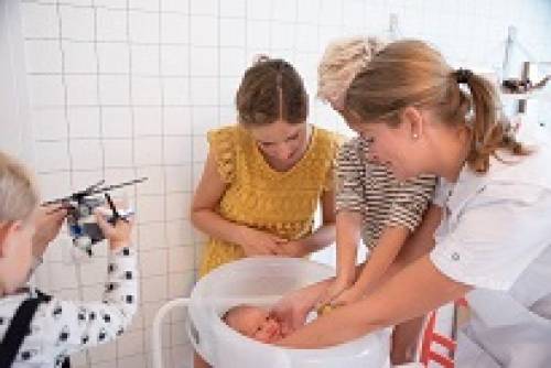 Een kraamverzorgende doet een baby in bad. Het gezin kijkt en helpt mee.