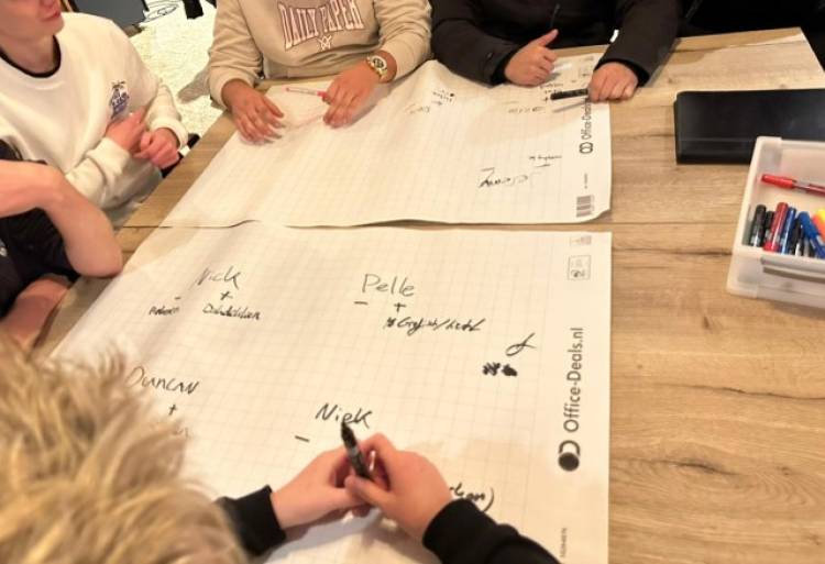 Handen en armen van jongeren die rond een tafel zitten met grote vellen geruit papier, terwijl ze stiften vasthouden