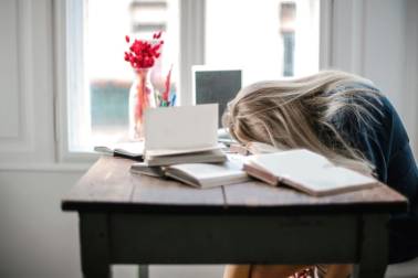 Meisje met hoofd op bureau en boeken om zich heen