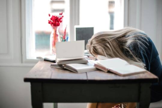 Meisje met hoofd op bureau en boeken om zich heen