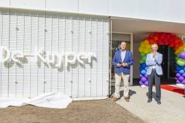 2 mensen van Stichting Leefomgeving Schiphol staan naast de gevel van het nieuwe buurtgebouw De Kuyper. Op de gevel staat de naam De Kuyper.