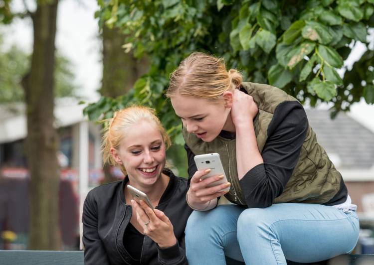 Twee meiden op een bankje kijken samen naar hun telefoon