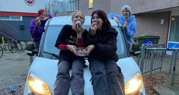 Vier jongeren eten oliebollen bij een auto