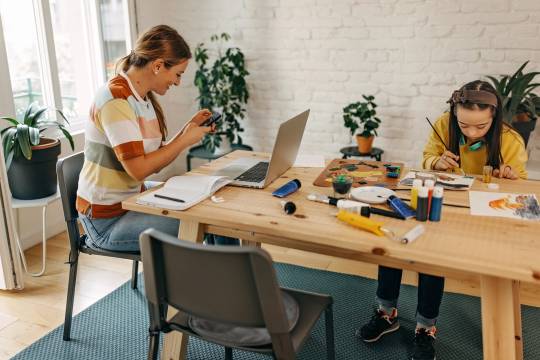 Decoratieve afbeelding: Je ziet een moeder aan het werk op haar laptop aan tafel. Naast haar zit een meisje te knutselen.