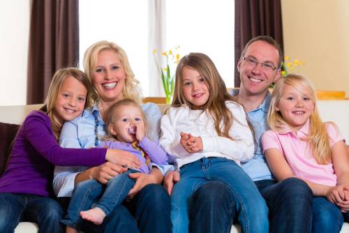 Twee ouders zitten met vier kinderen thuis op de bank