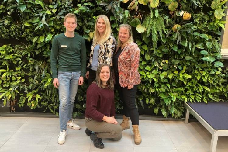 Babette, Elzemieke, Dirk en Daniek van de gemeente West Betuwe poseren voor een groene plantenmuur en kijken lachtend in de camera