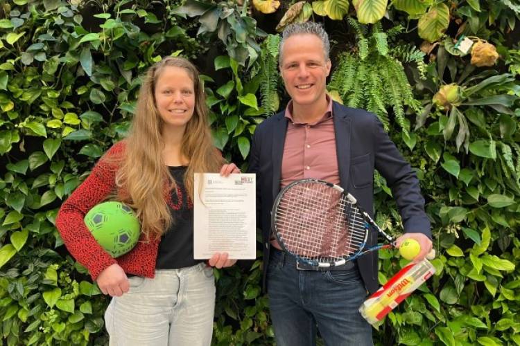 JOGG-regisseur West Betuwe Ans van 't Pad staat naast wethouder Rutger van Stappershoef. Samen houden zij de JOGG-overeenkomst in de lucht, terwijl ze sportspullen vasthouden.