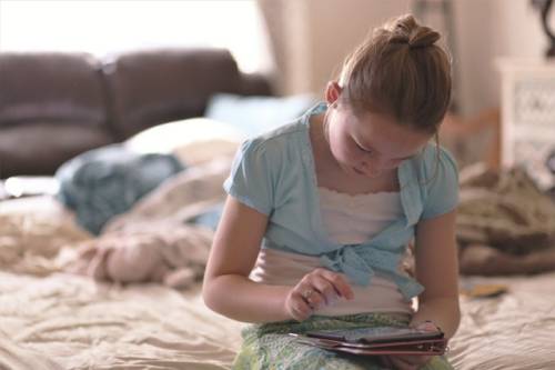 Een meisje zit op een bed terwijl ze een tablet bedient
