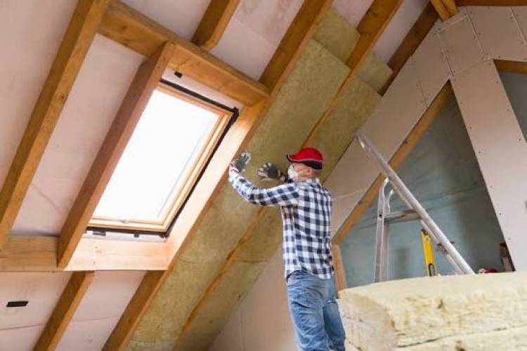 Man op trap bevestigt isolatiemateriaal tegen het plafond van een zolderkamer.