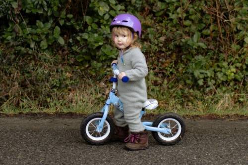 Een peuter gebruikt een loopfiets en draagt een helm
