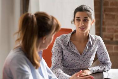 Een vrouw met een gestipt overhemd is in gesprek met een andere vrouw