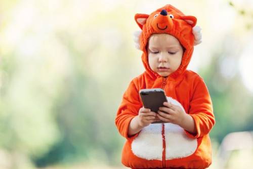 Een peuter in een dieren-verkleedpak houdt een smartphone vast