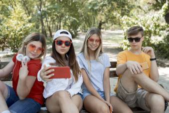 Decoratieve afbeelding: Vier tieners op een bankje. Ze maken een selfie.
