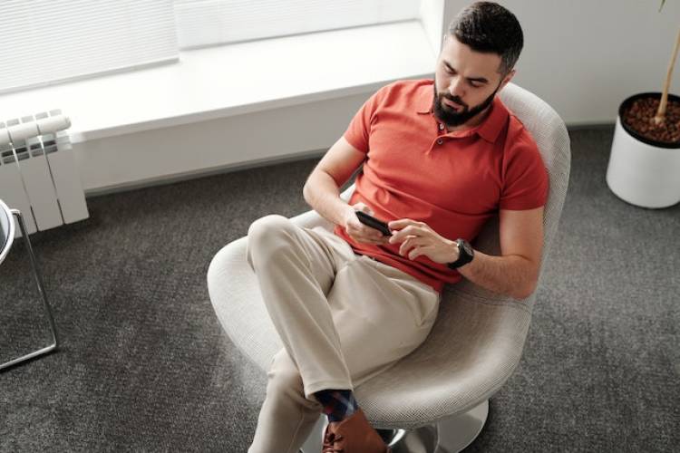 Een man zit in binnen in een stoel en bedient een smartphone