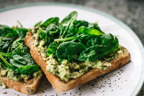 Een boterham belegd met geprakte avocado en veldsla