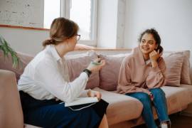 Een jongere en een therapeut zitten pratend op een bank