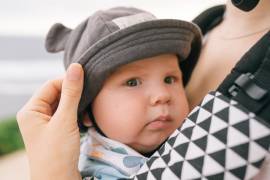 Een baby zit in een draagzak en kijkt in de camera