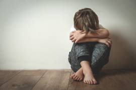 Een jongen in de basisschoolleeftijd zit op de vloer, tegen de muur aan, met opgetrokken knieƫn en met zijn hoofd in zijn armen