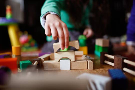 Decoratieve afbeelding: Een foto van een bouwwerk van blokjes. Je ziet een kinderhand die aan het bouwen is.
