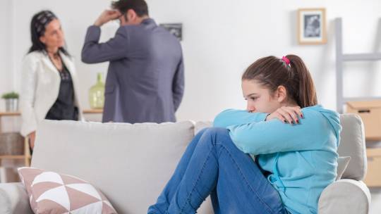 kind zit op de bank, ouders maken ruzie op de achtergrond